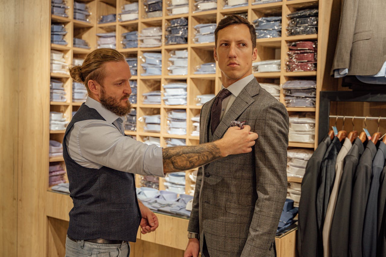 A tailor assists a man with a suit jacket fitting in a clothing store.